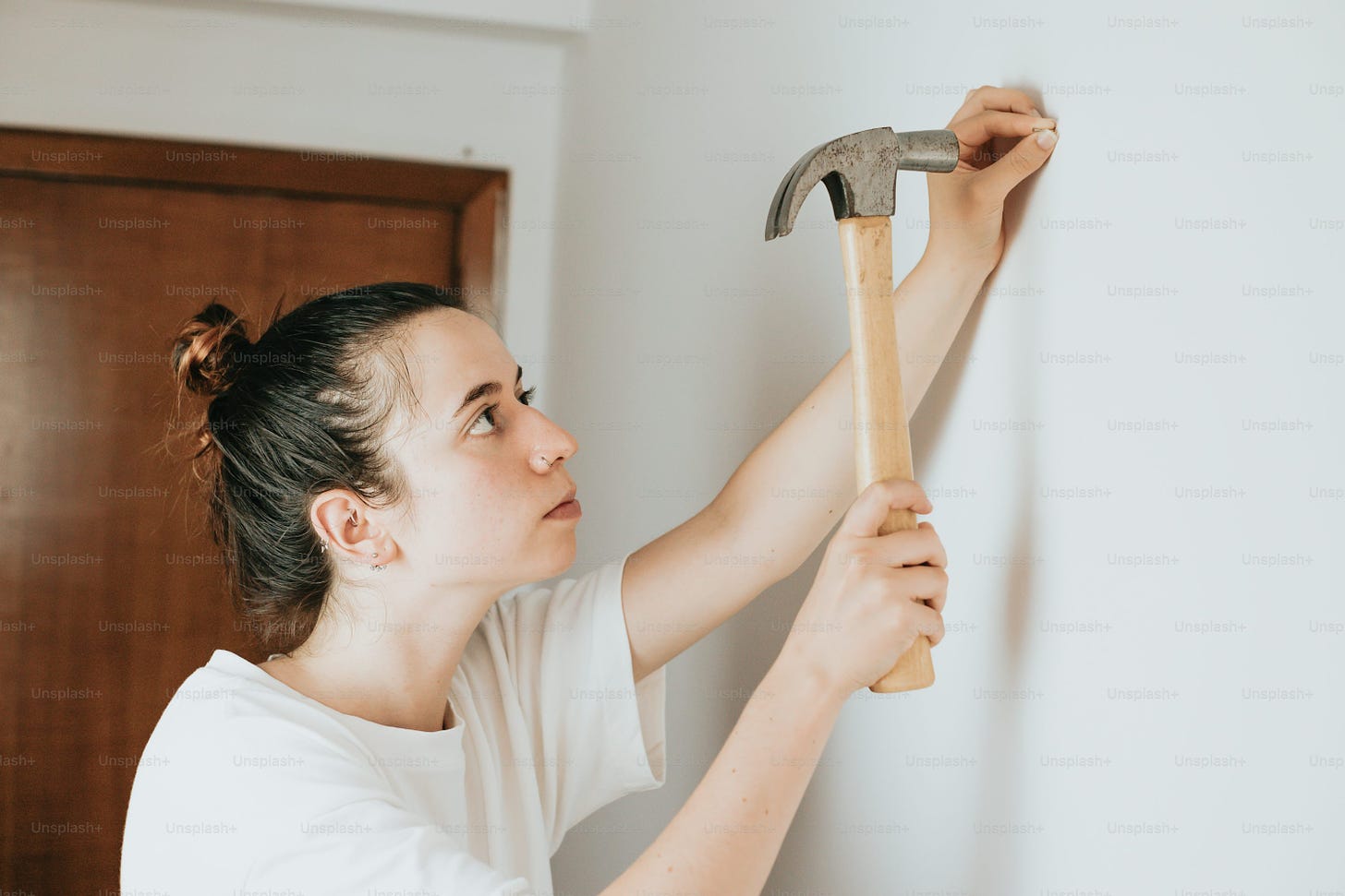 a woman holding a hammer up to a wall