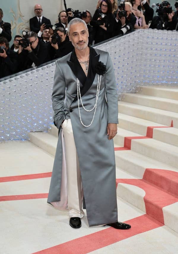 wearing a satin trouser with a floor-length suit jacket with a rose broach with pearls
