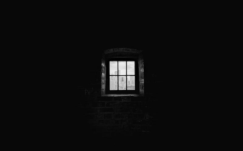 A small solitary barred window in a dark room