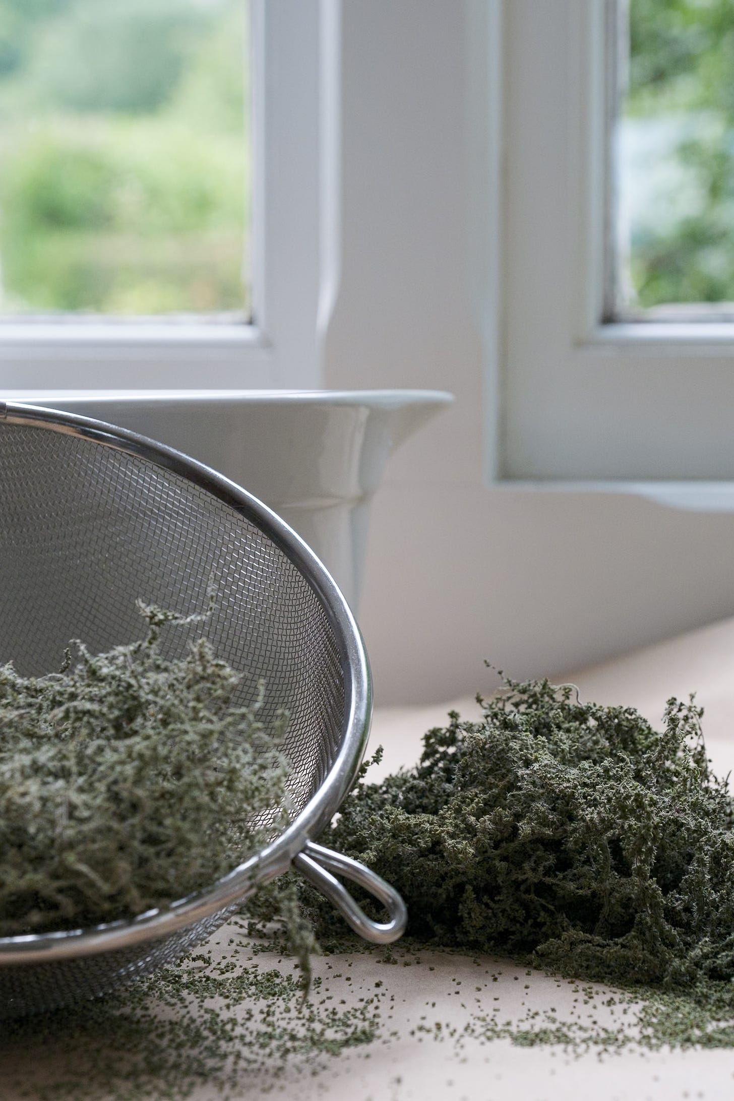 Dried nettle seeds on brown paper and in sieve in front of white wooden framed window