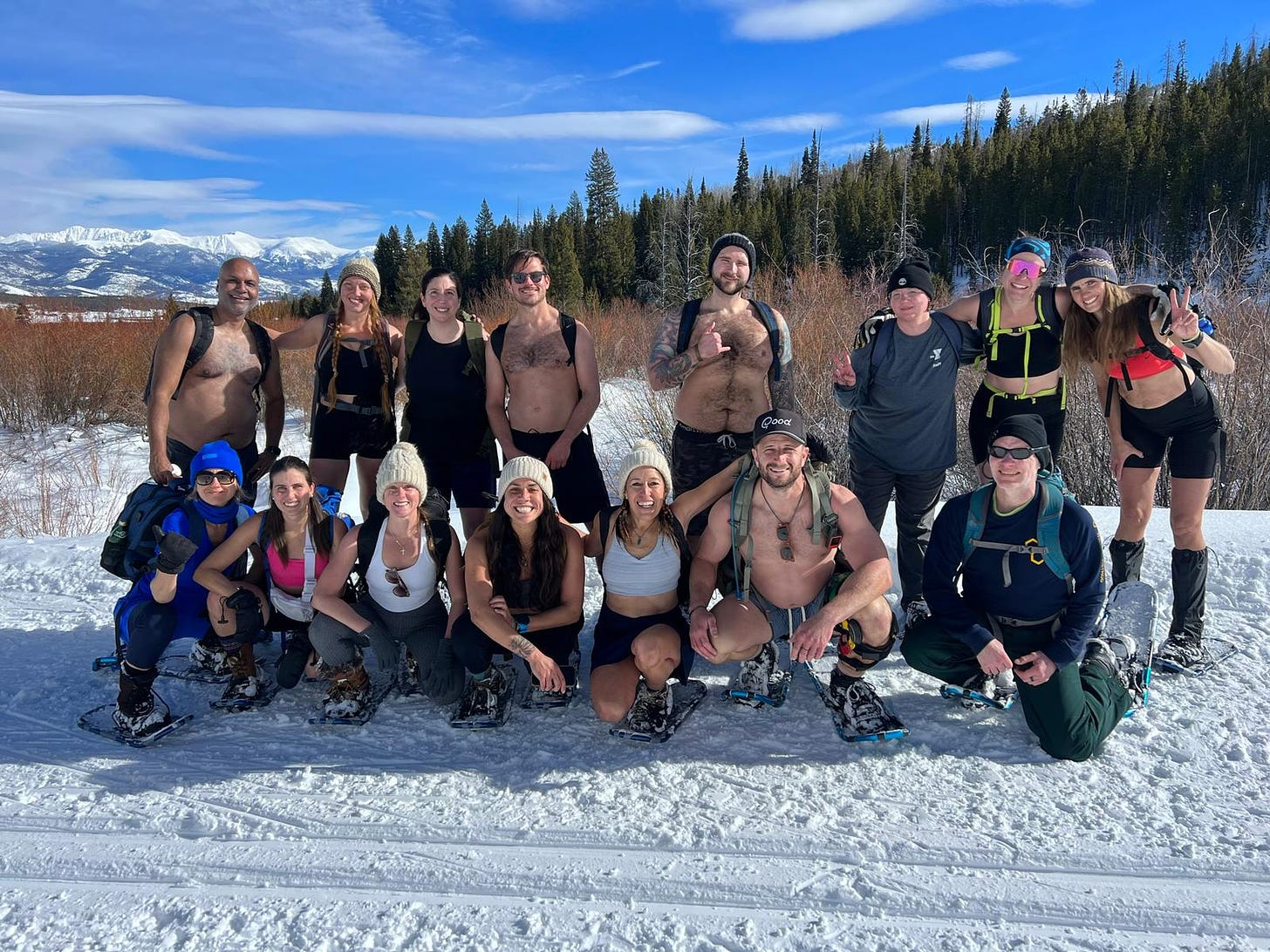 Group photo of happy people in snowshoes and minimal athletic clothes, mountains in background