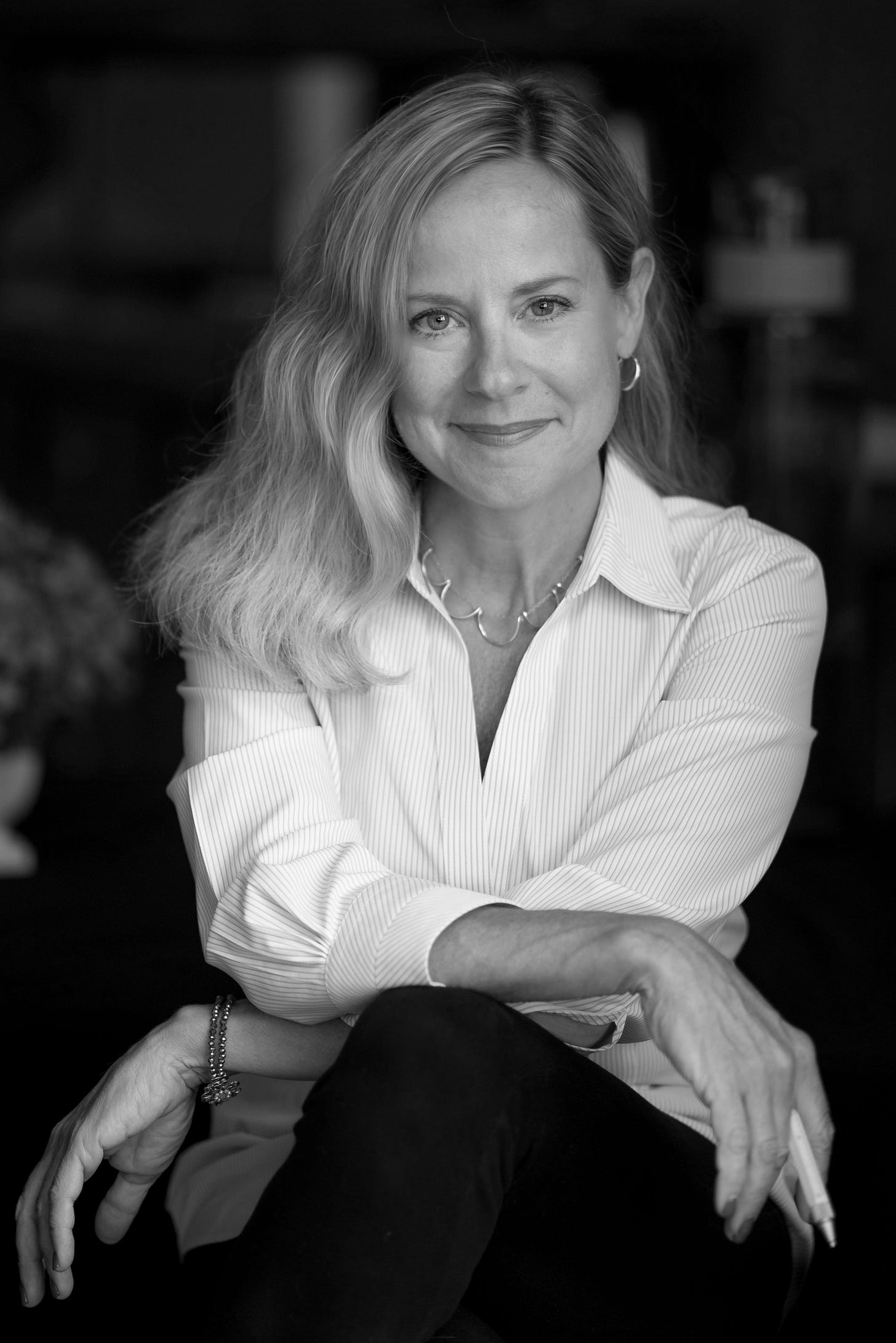 black and white image of blonde woman in white, button-downed shirt with arms crossed and holding a pen