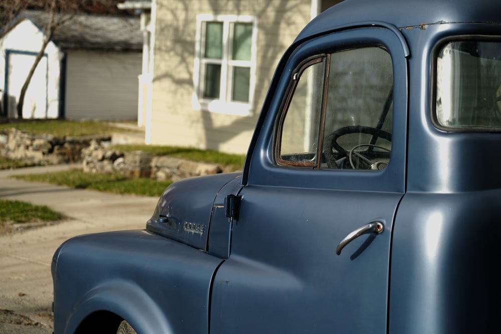 A navy blue 1950s pickup gleams in the sunshine in front of pale green house in Helena, Montana. 