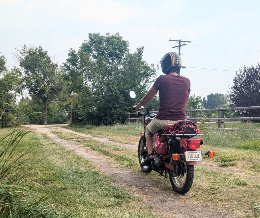 a woman riding down a dirt driveway on a motorbike