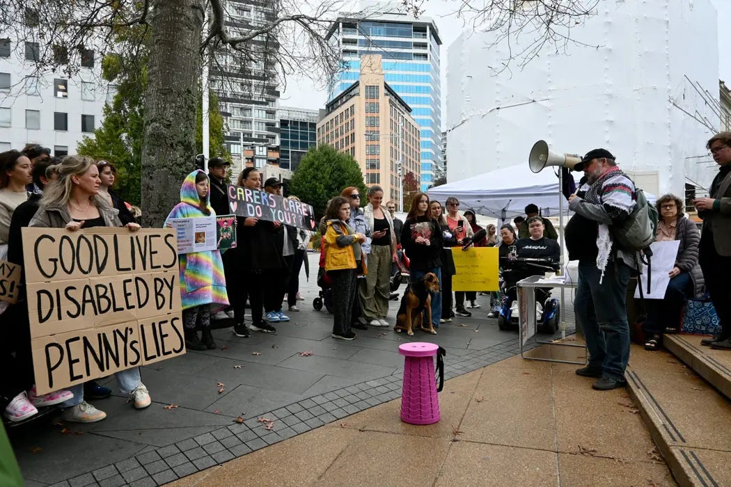 A photo of a protest against Whaikaha's withdrawal of flexible funding, organised in April last year by System Change Aotearoa. Image shows a blind activist speaking to the gathered crowd at Aotea Square, Auckland. A photo of a protest against Whaikaha's withdrawal of flexible funding, organised in April last year by System Change Aotearoa. Image shows a blind activist speaking to the gathered crowd at Aotea Square, Auckland.