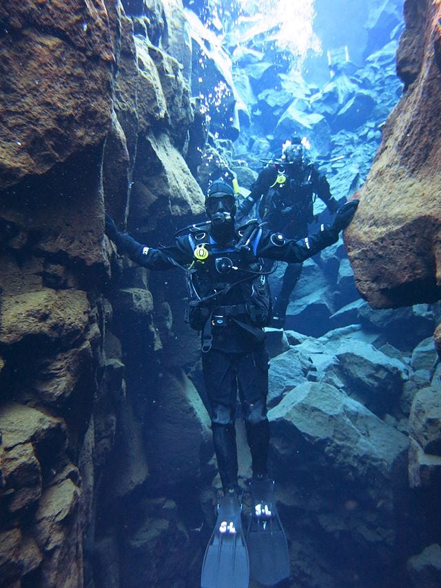 Divers touching the edges of 2 tectonic plates at Silfra Fissure, Iceland
