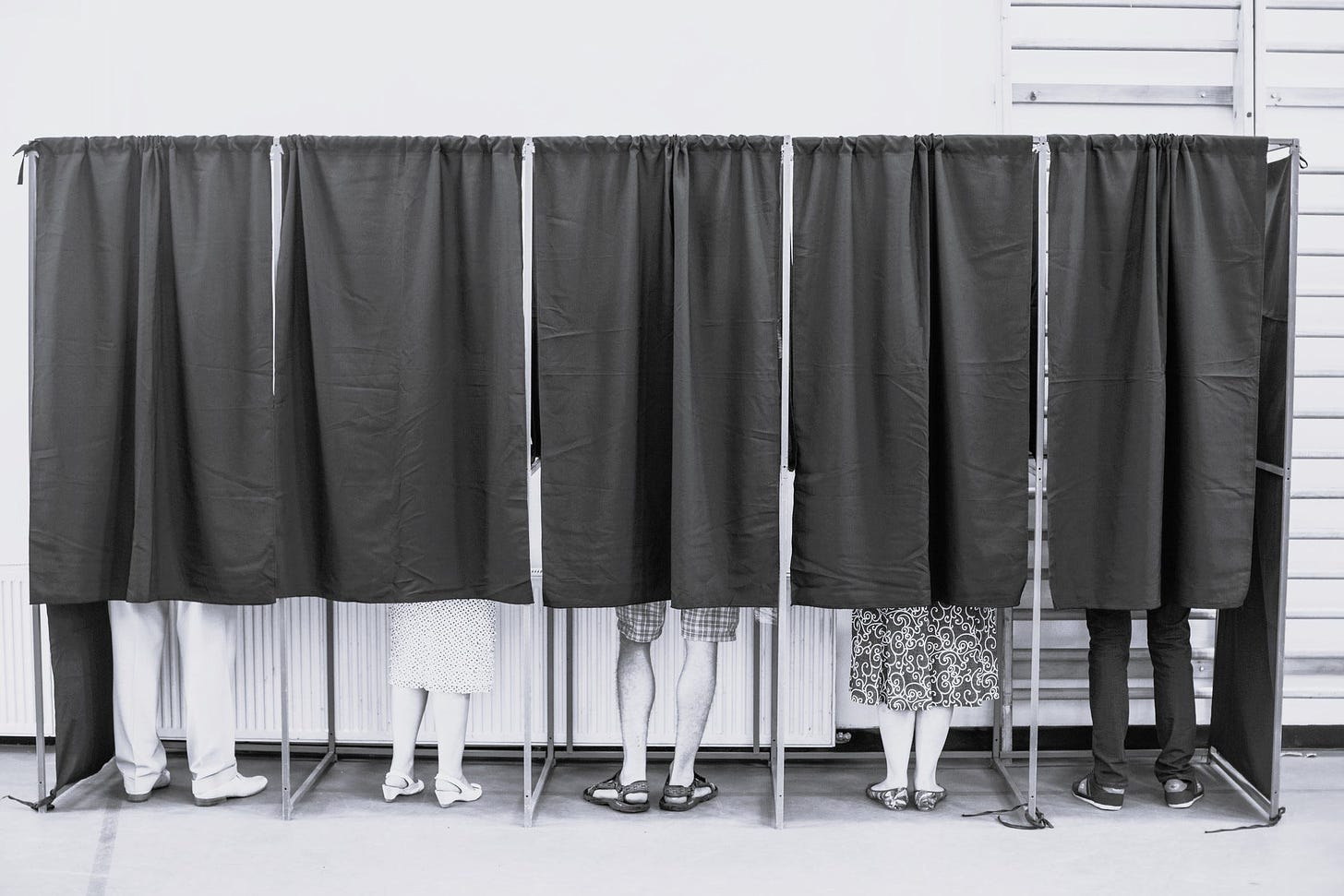 Image of voters inside booths with closed curtains. Only their feed are showing at the bottom.