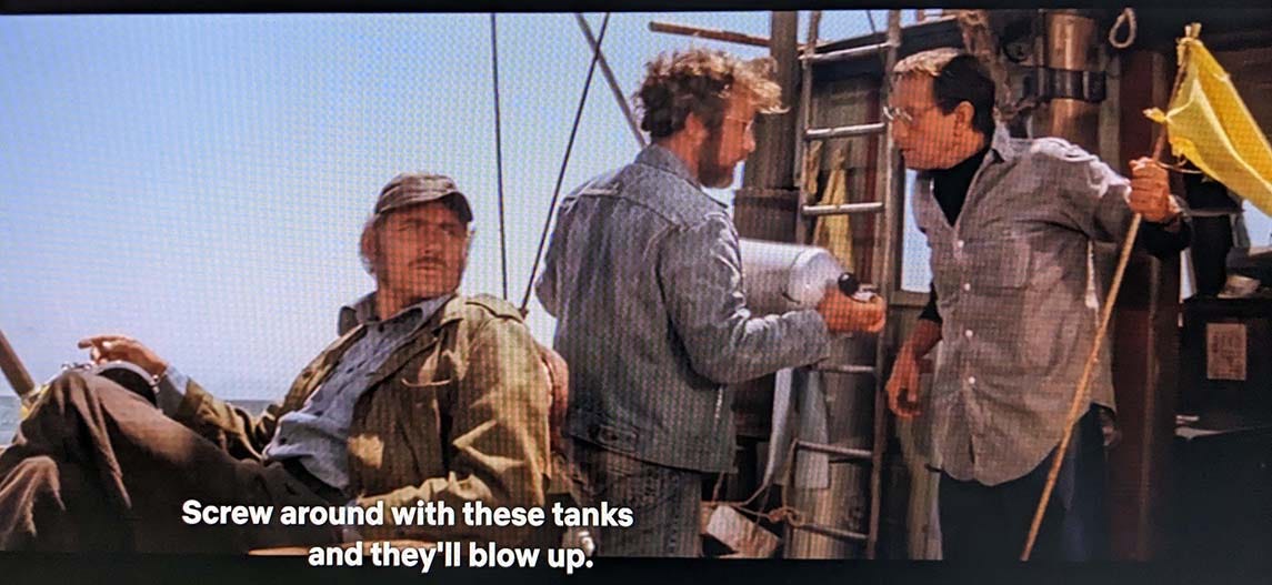 A still from Jaws: Three men on a boat. One man, Cooper is saying 'Screw around with these tanks and they'll blow up!'