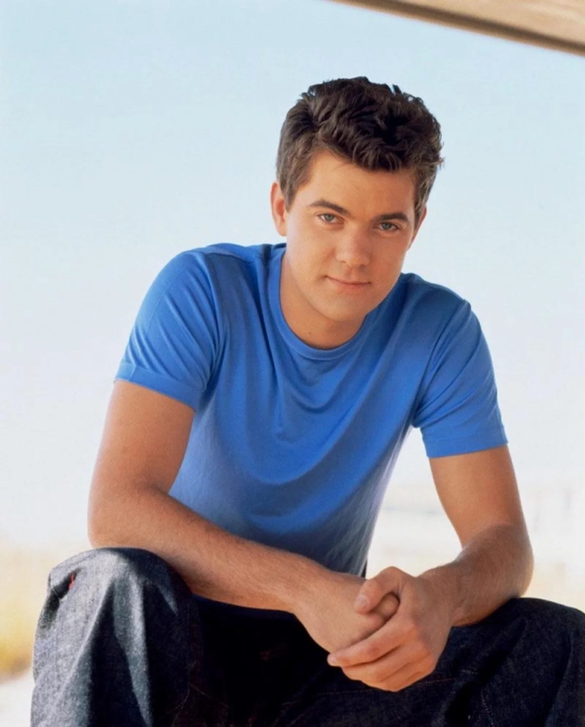 A teenage boy in a blue shirt with brown hair and a smolder-y look stares at the camera with his arms in a sexy kind of casual "I'll always be here for you" kind of stance.