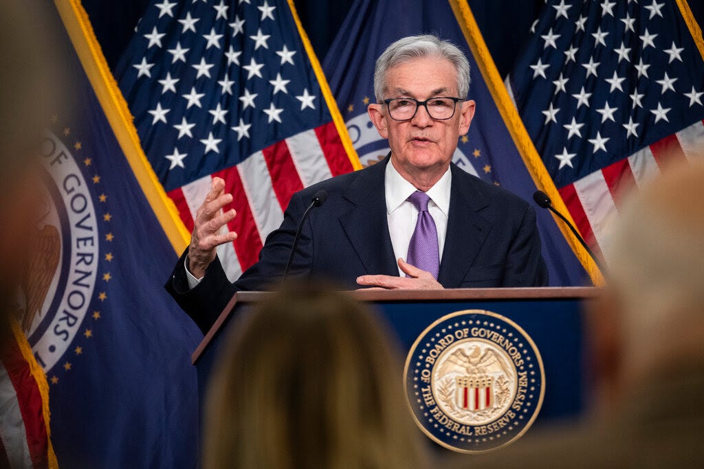Jay Powell, the Fed chair, in a dark suit, white shirt and purple tie, standing at a lectern in front of U.S. flags.