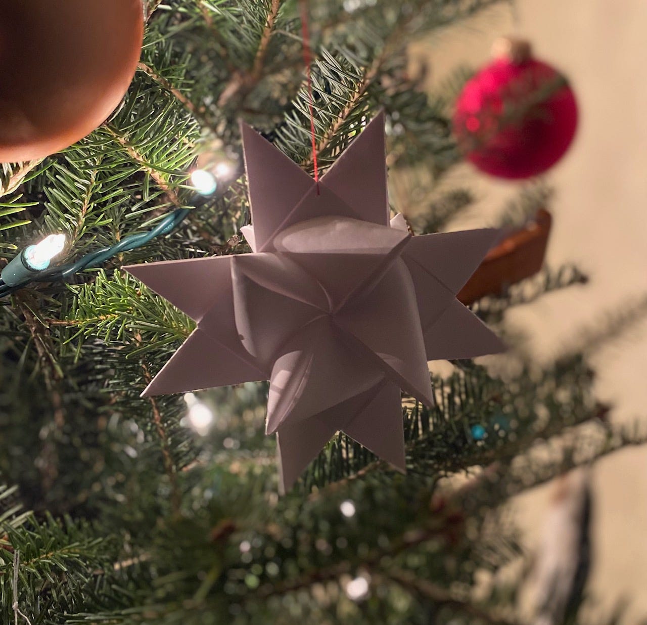White paper folded Swedish star hanging on tree with twinkly lights.