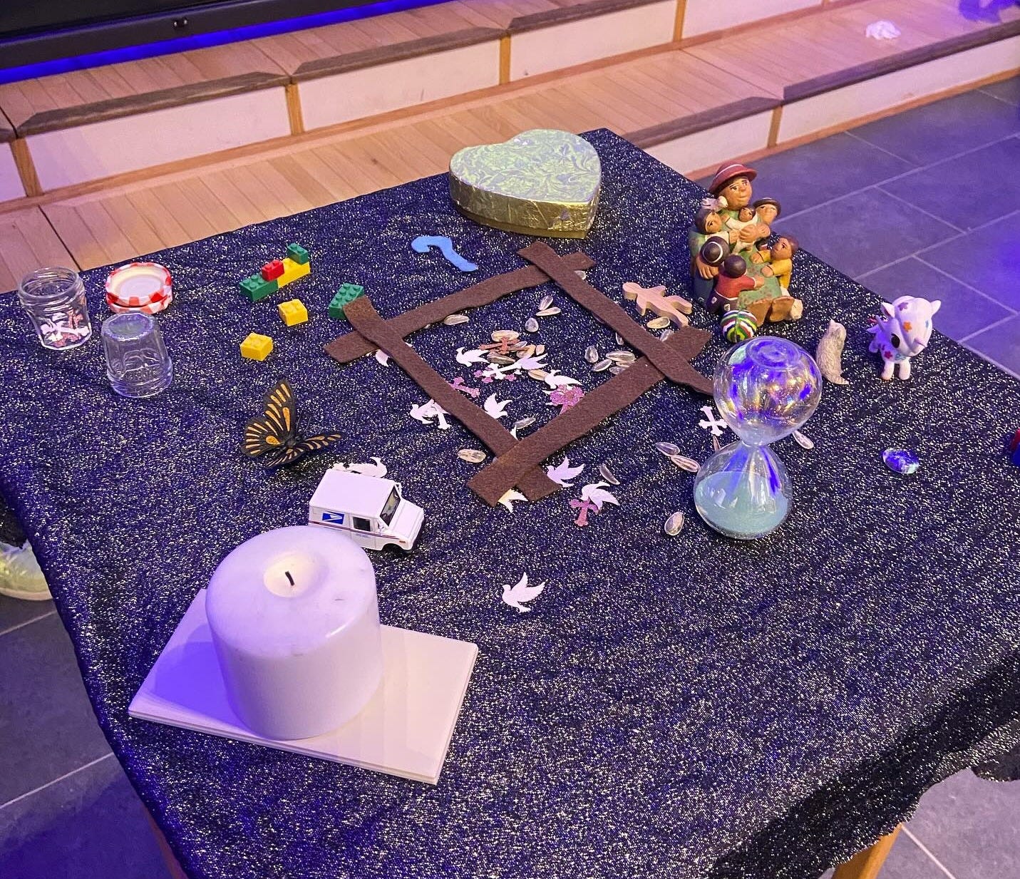 A variety of small objects including a plastic butterfly, a gold box shaped like a heart, sunflower seeds, legos, and confetti are spread on a table. A variety of small objects including a plastic butterfly, a gold box shaped like a heart, sunflower seeds, legos, and confetti are spread on a table.