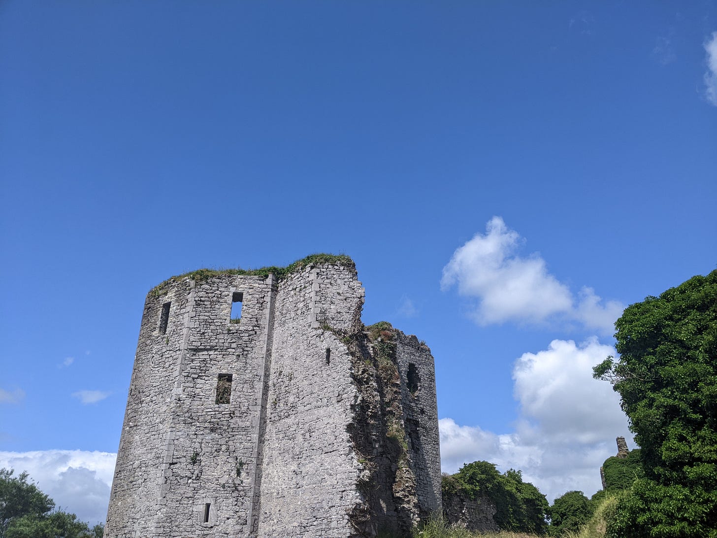 A patially ruined stone castle tower stands against out against a blue sky and green ivy.