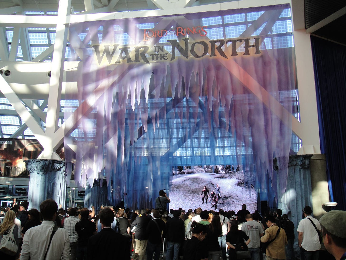 A large crowd at a conference gathers in front of a display for the video game The Lord of the Rings: War in the North
