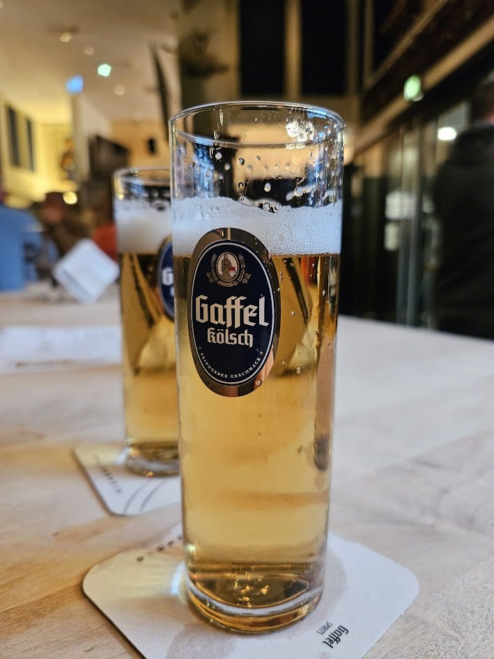 Two glasses of pale Gaffel kolsch. The glasses are printed with the navy blue and silver logo of the brewery.