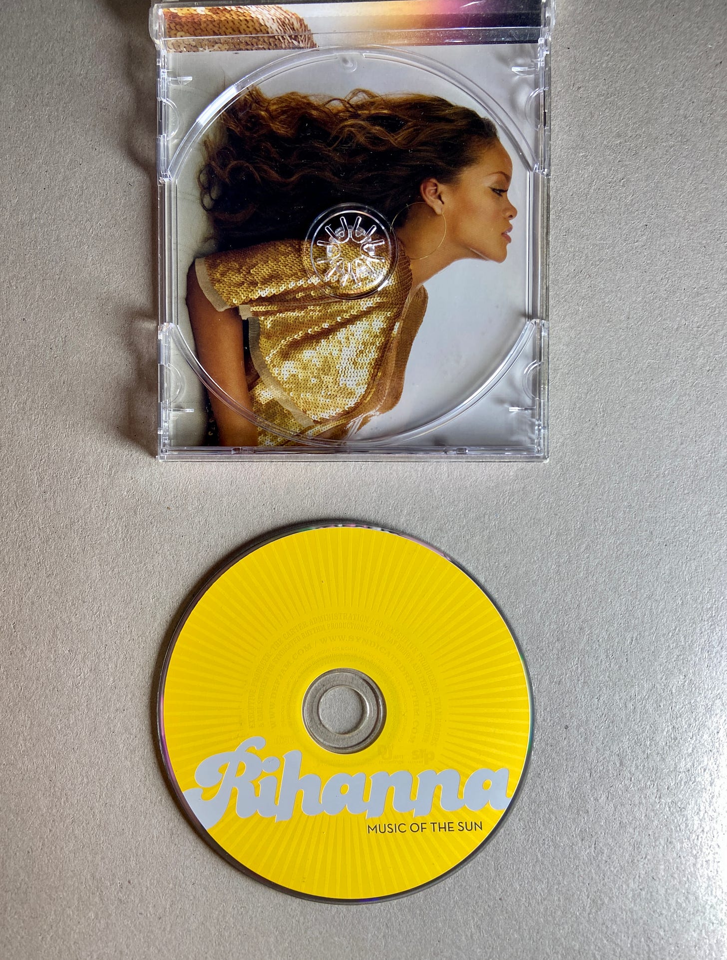 the inside of the jewel case for Rihanna's Music of the Sun album; she leans back while wearing a gold sequin top. the yellow CD lays below the case.