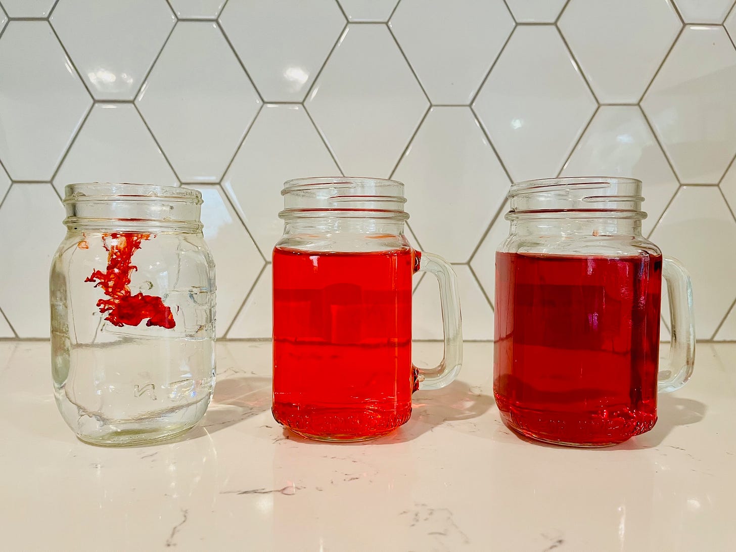 three glass cups of water, the first has a drop of red food coloring billowing out into the water, the next two glasses are full of red liquid