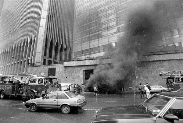 A plume of smoke rises from a building with fire engines parked out front.