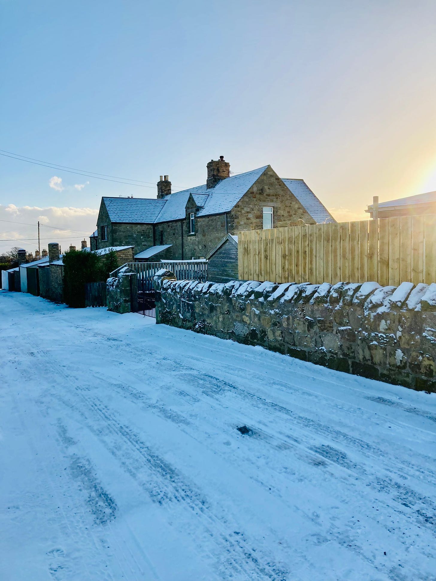 Snowy day in Northumberland. Snow covers stone fence and homes golden sunlight floods in.