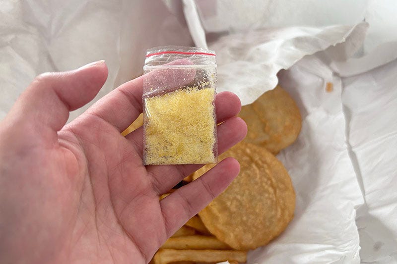 Hand holding a bag of chicken salt over fish and chips.