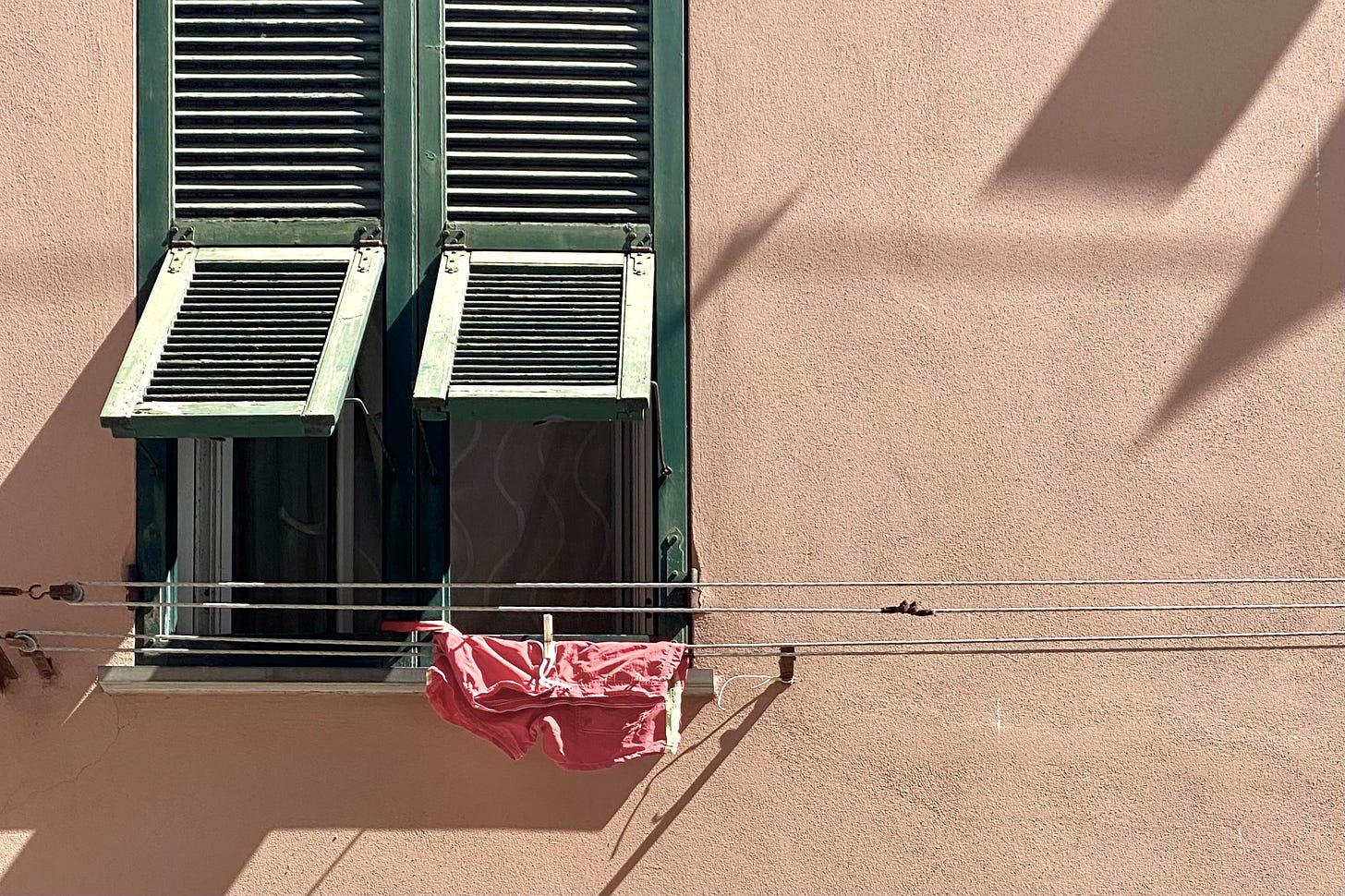 A window in Italy where washing is hanging outside. It's red shorts on a washing string.