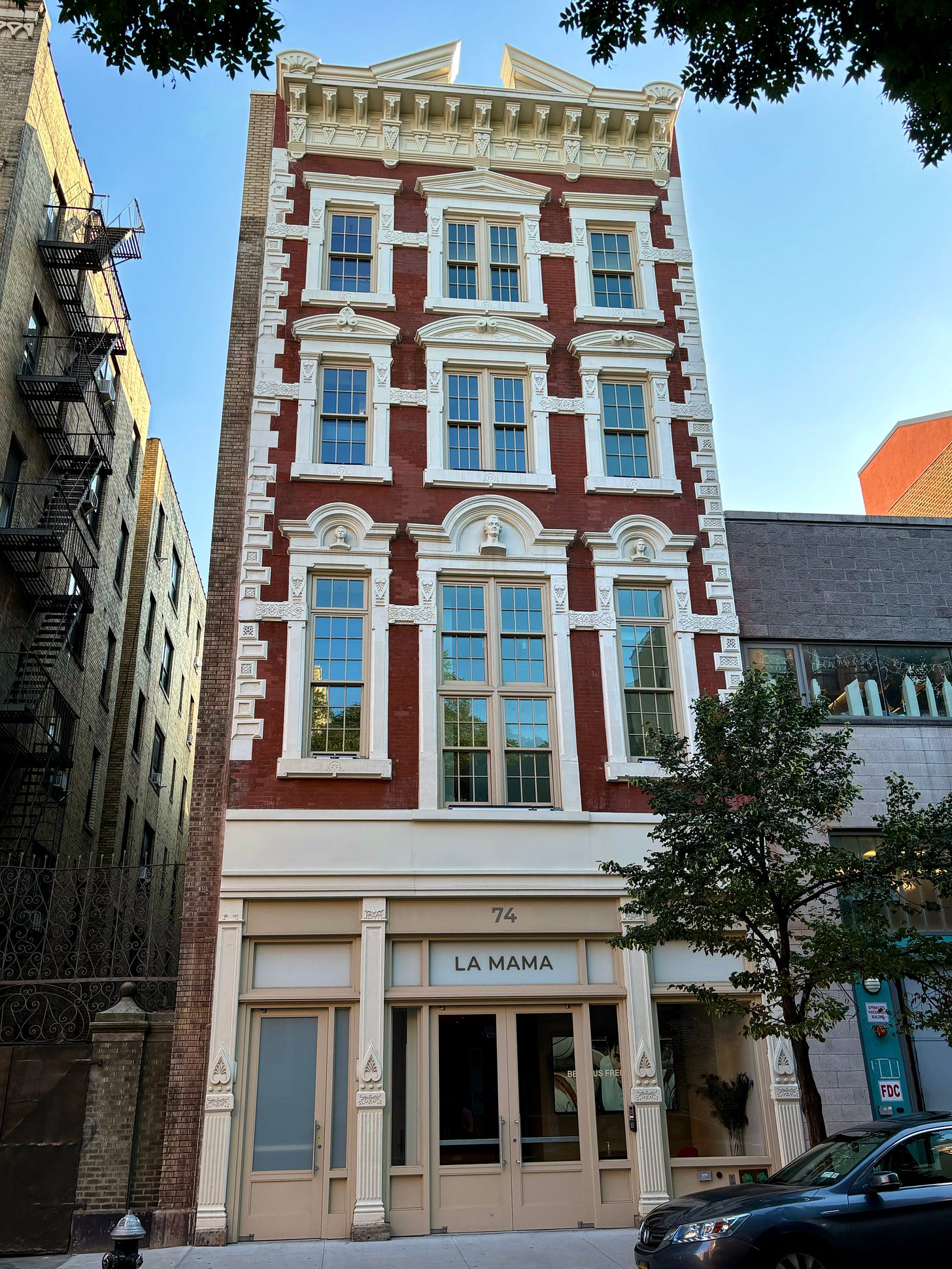 LaMama at 74 East 4th Street, a red brick building with white trimmed windows and busts of Mendelssohn, Mozart, and Beethoven.