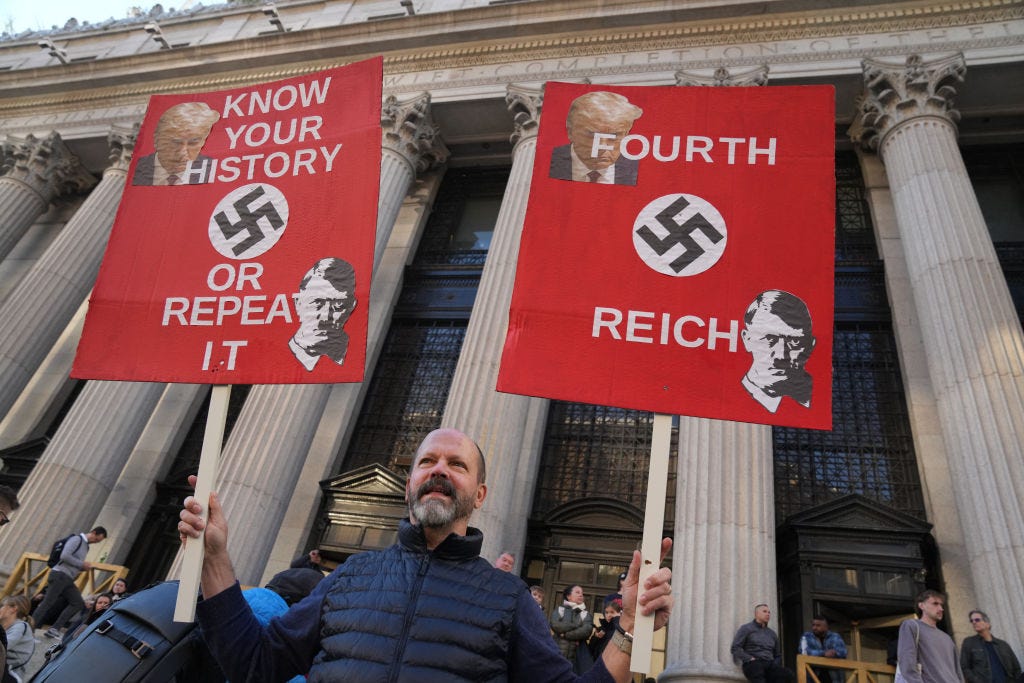 A protester in front of Madison Square Garden in New York City holds up two placards comparing Donald Trump to Adolf Hitler; text on the sign reads "Know your history or repeat it" and "Fourth Reich."