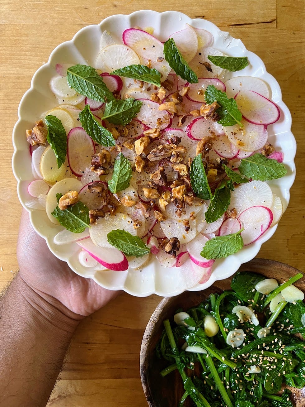 A hand holding a plate of a radish, mint and walnut salad