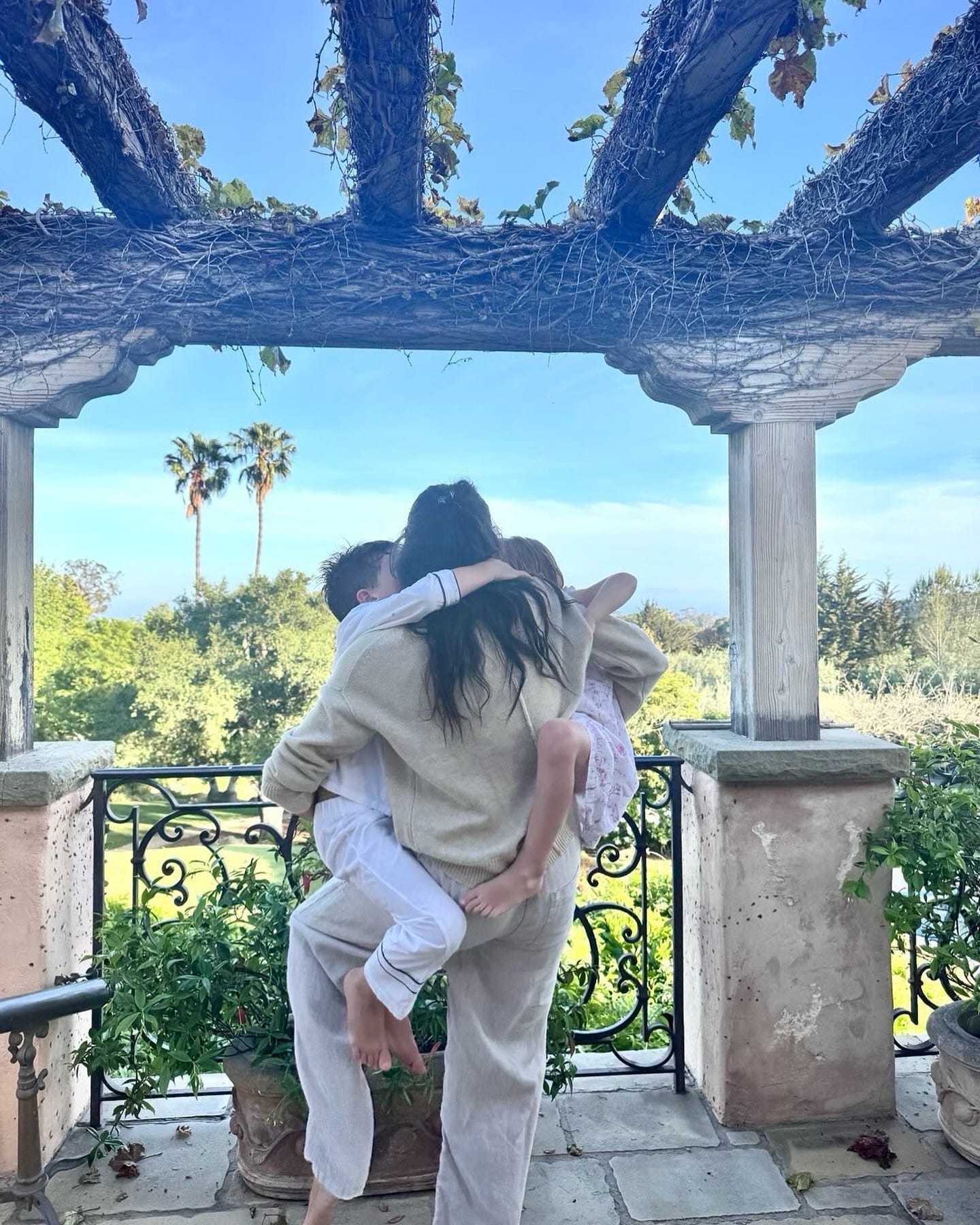 Meghan Markle holding her two children facing away from the camera on bedroom terrace