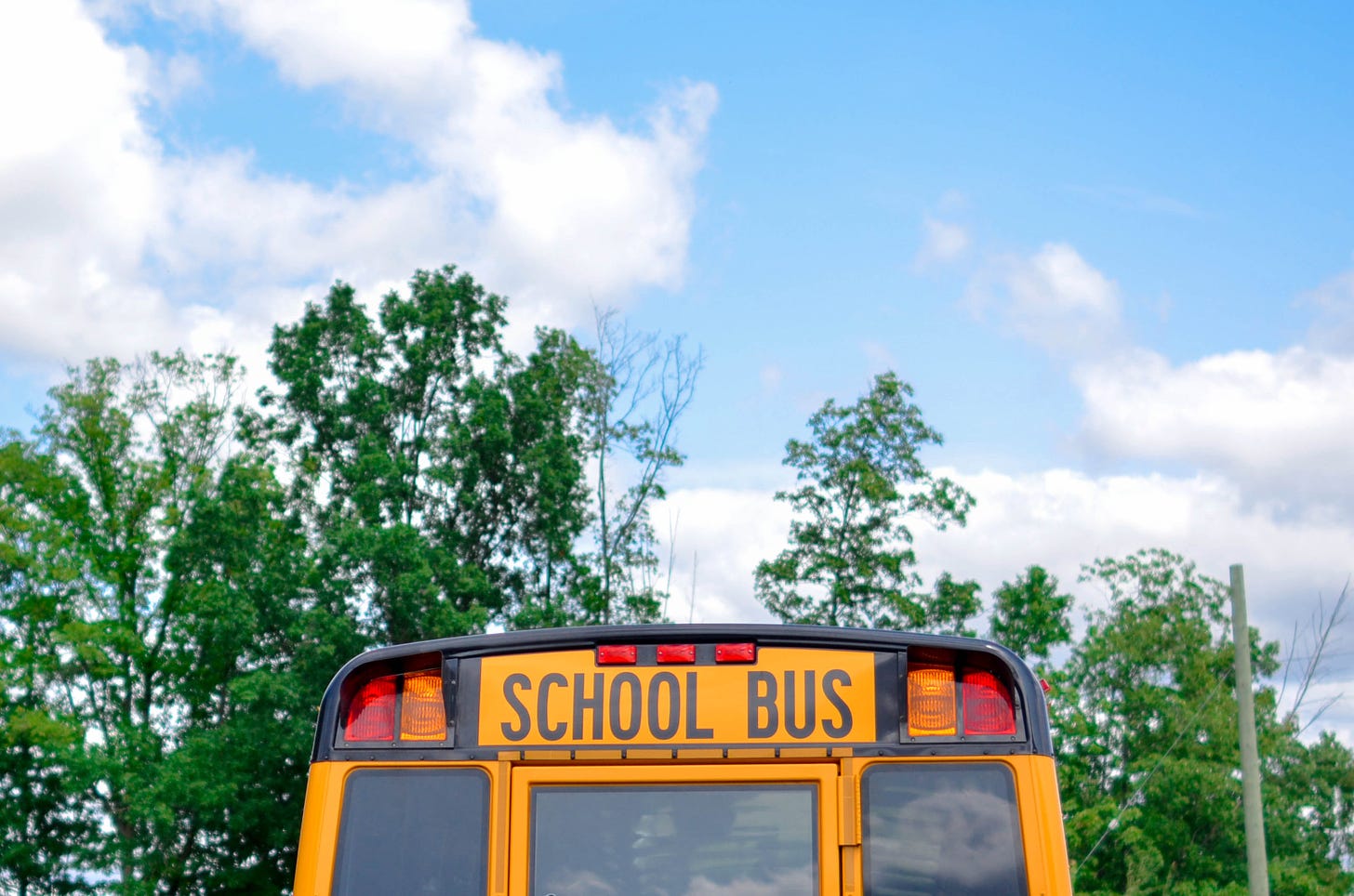 the back of a school bus under a blue sky with clouds