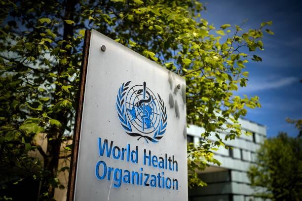 Photo of the World Health Organization's sign post near their office in Switzerland with a background of a tree and a blue sky Photo of the World Health Organization's sign post near their office in Switzerland with a background of a tree and a blue sky
