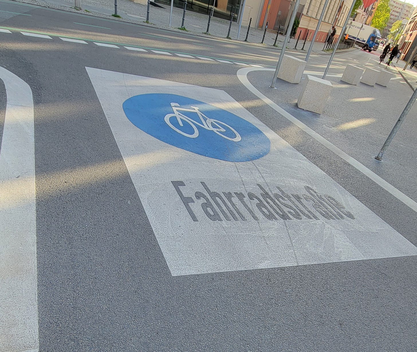 Painted image on street surface, white rectange with a blue circle in the middle. Inside the blue circle is the outline of a bicyle in white. The word Fahrradstraße is written in black below.
