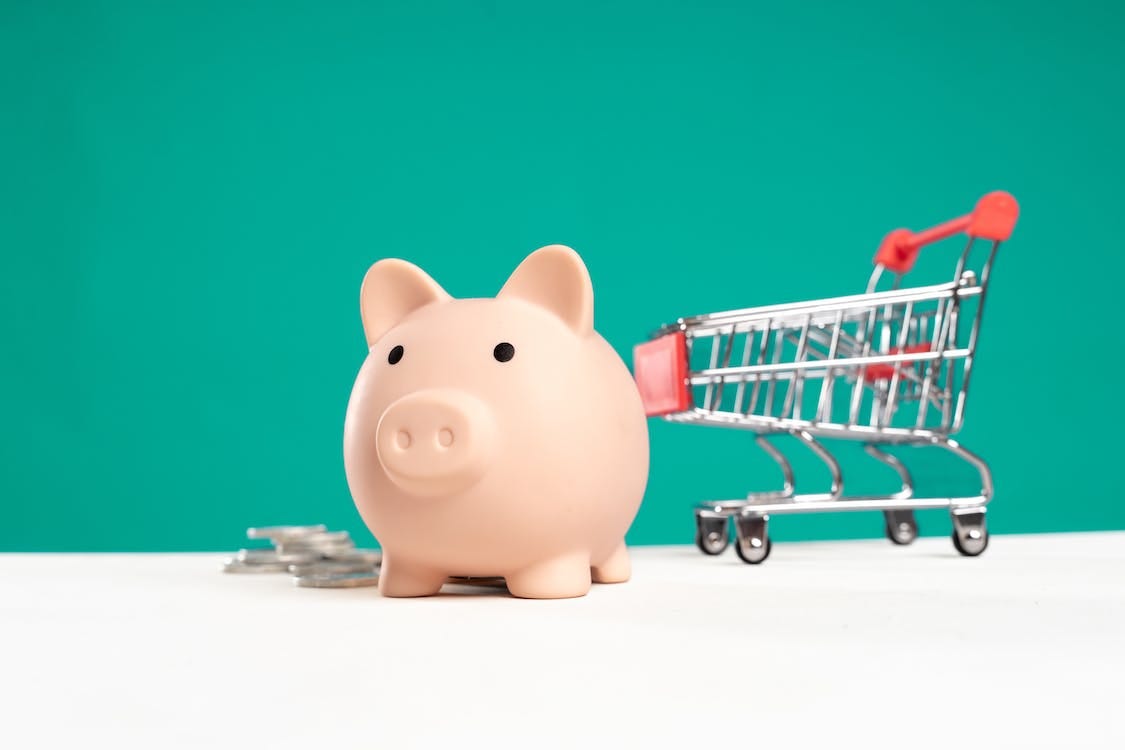 Stock photo of pink piggy bank with a mini shopping cart behind it.