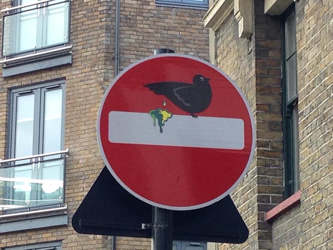 Street art on a traffic sign of a bird pooping