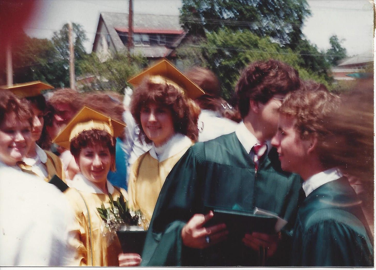 A blurry photo of high school students in caps and gowns, diplomas in hand, pose with their friends