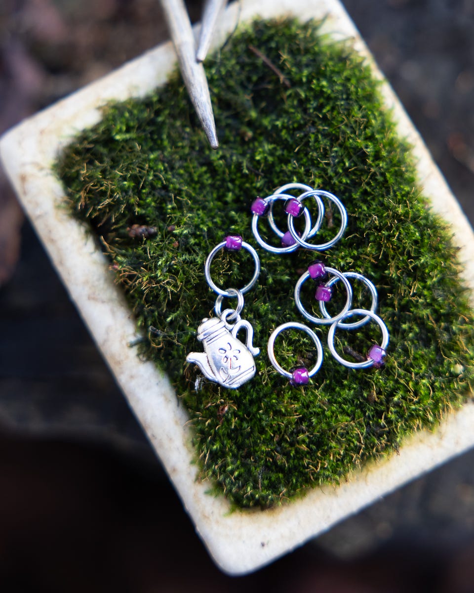 Set of beaded ring stitch markers, arranged on a small pot of moss