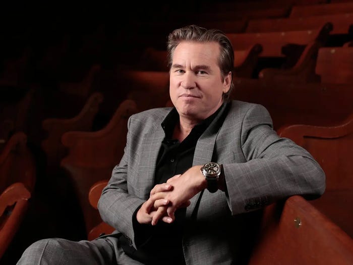 Val Kilmer posing for a portrait while sitting in an empty movie theatre.