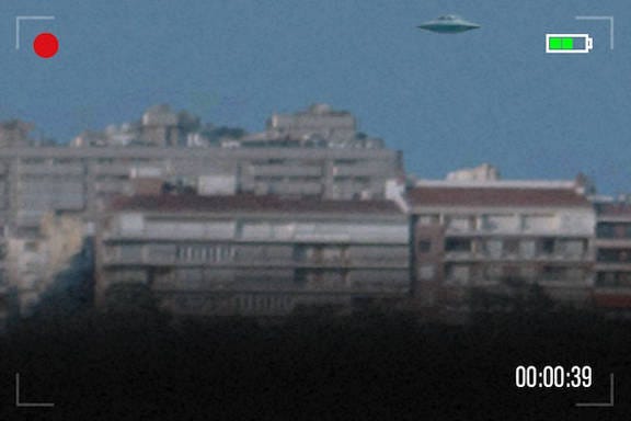 A UFO hovers over an apartment block. Image is blurry and has camcorder aesthetics.