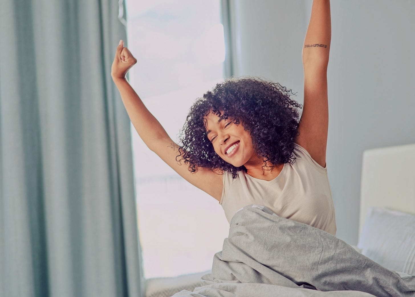 Young woman sitting up in bed smiling and stretching