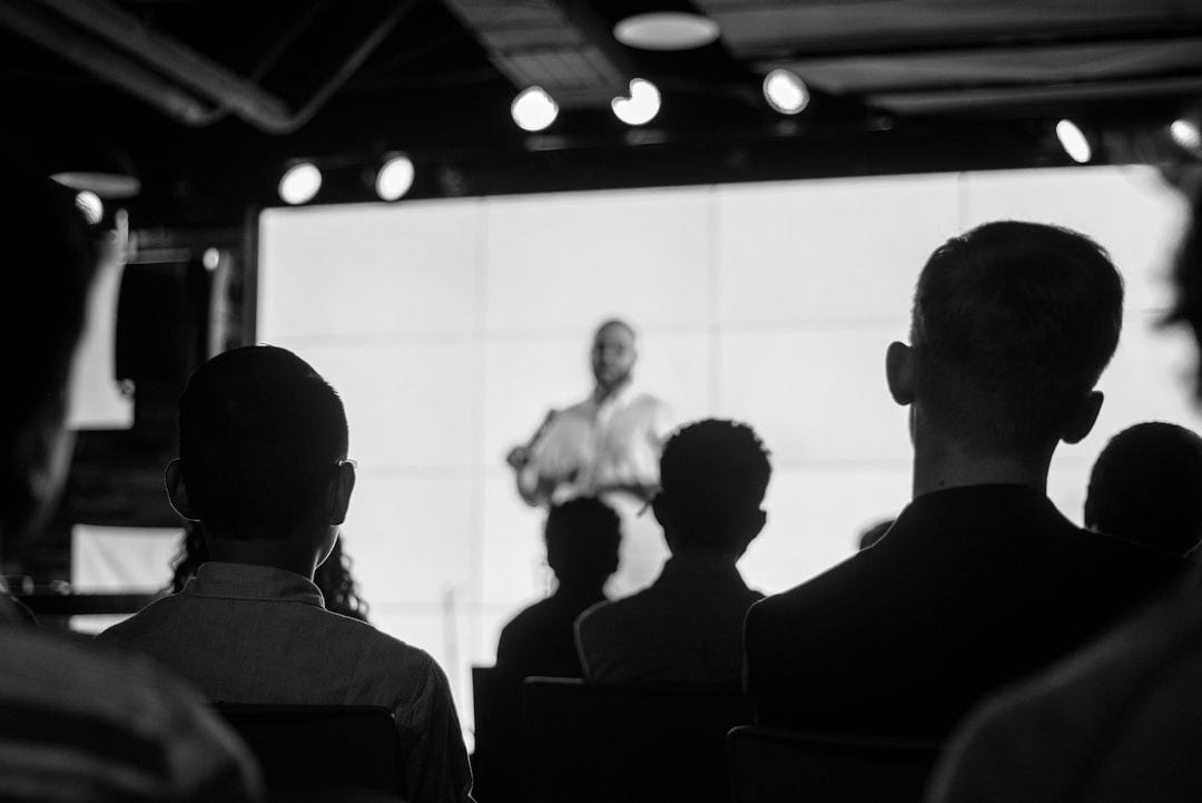 man in black suit standing in front of people man in black suit standing in front of people