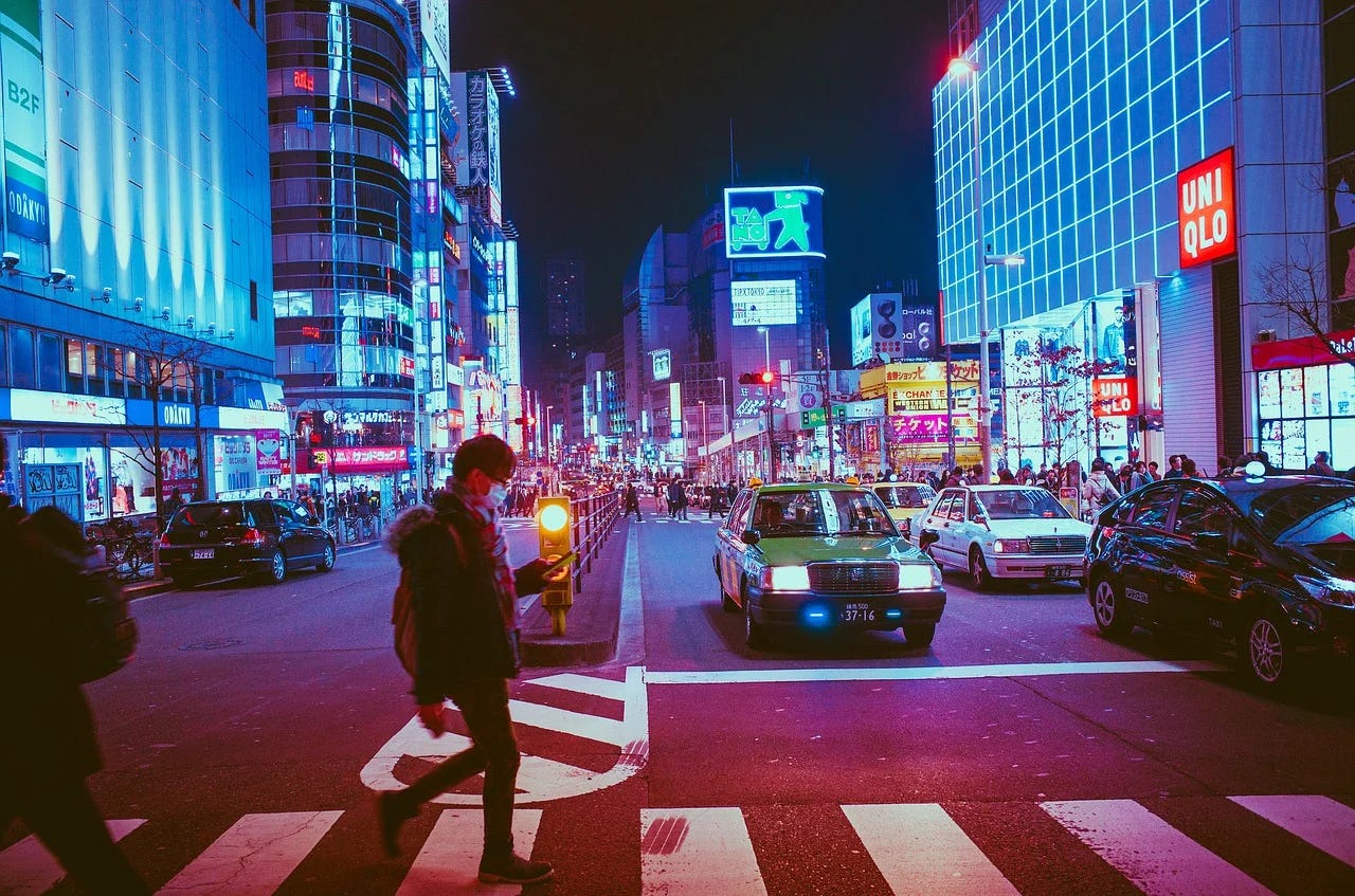 A man crossing the road in a busy lit-up district in Osaka, Japan, at night