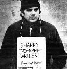 Middle aged writer Crad Kilodney wearing toque and jacket outside with sign around his next that says no name writer buy my book $2