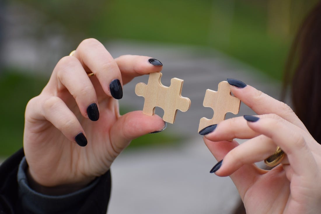 Two hands, both holding a wooden puzzle piece each which fit perfectly together.