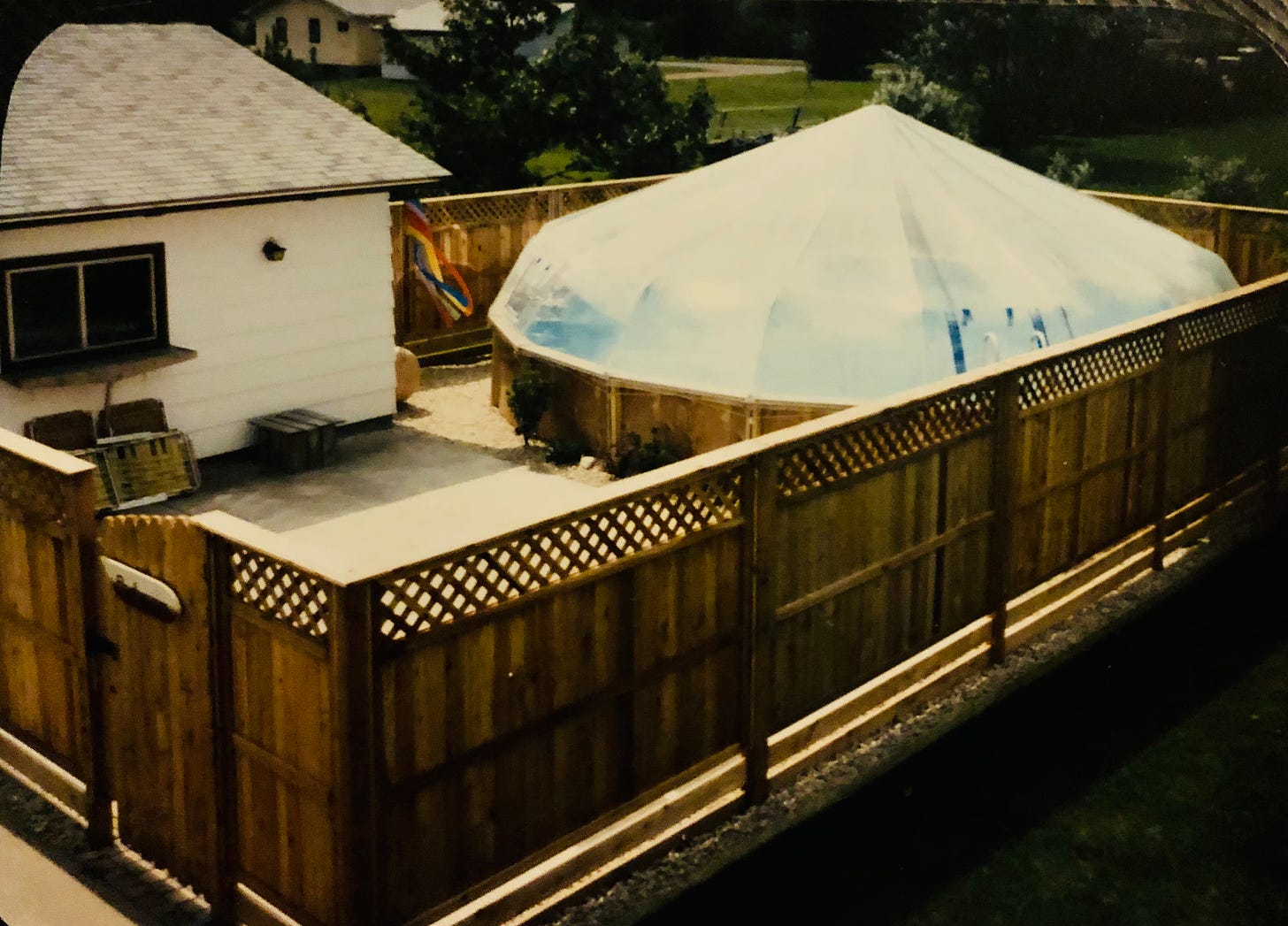 A domed pool sits inside a lovely fence next to the garage. To the right, one small strip of lawn remains.