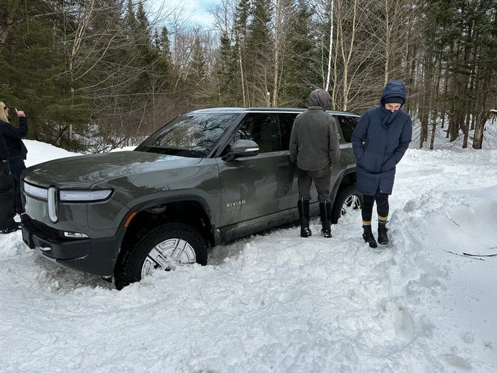 An image of Chase Merrill's Rivian stuck in a snow drift with several people looking at it.