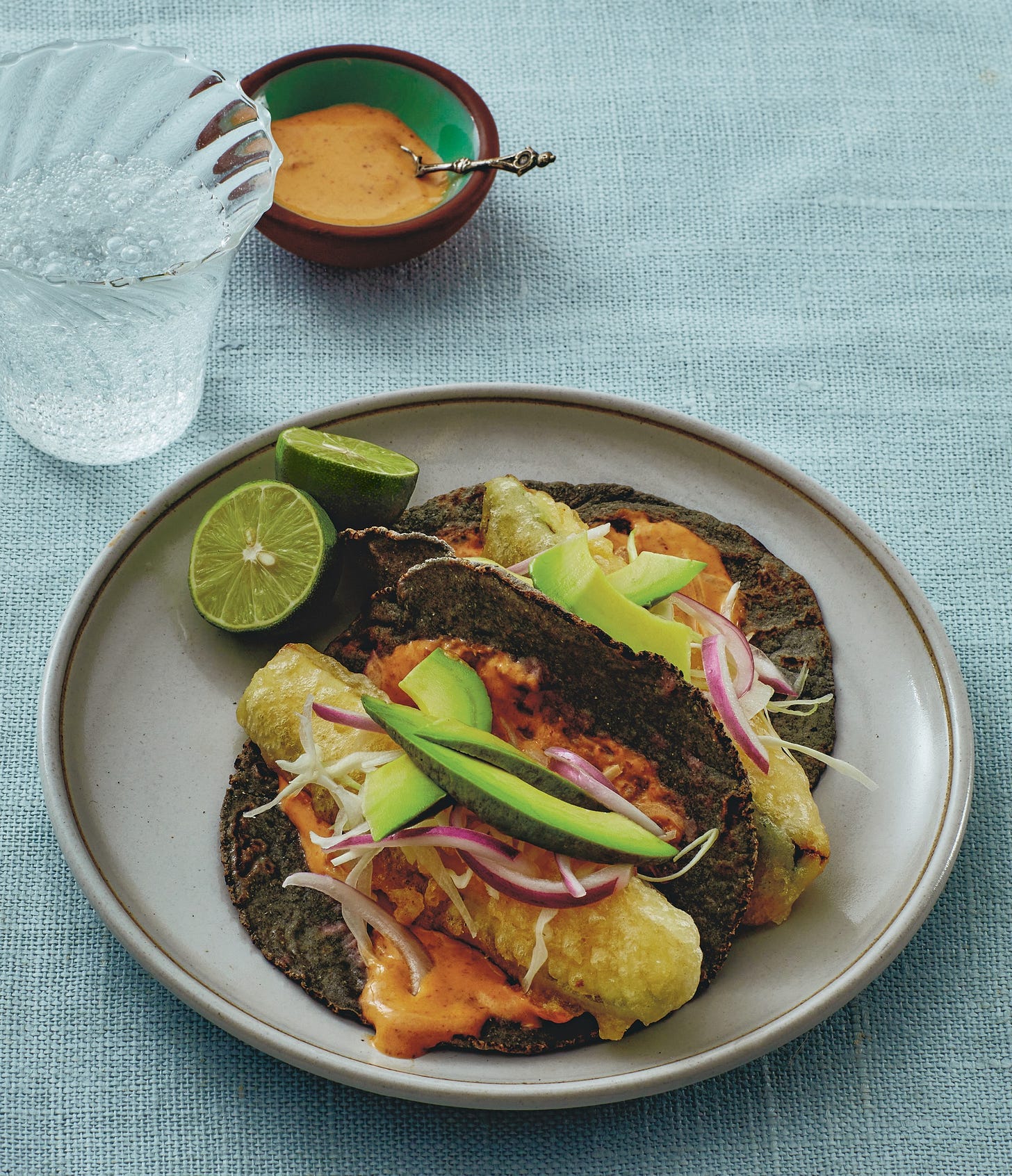 Fried zucchini "fish" tacos on a plate with pale blue tablecloth.
