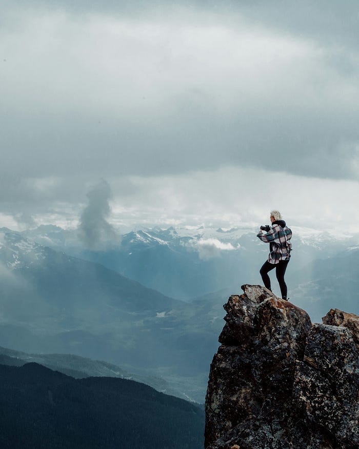 Individual standing at the top of a mountain taking a photograph.