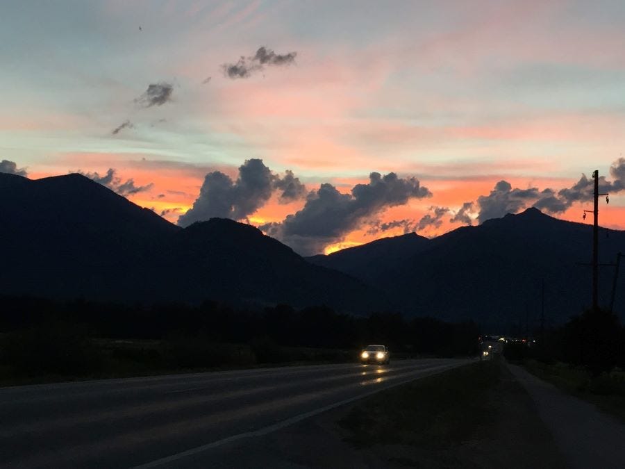 a dark sunset scene, with mountains in silhouette and cars with their headlights on the road