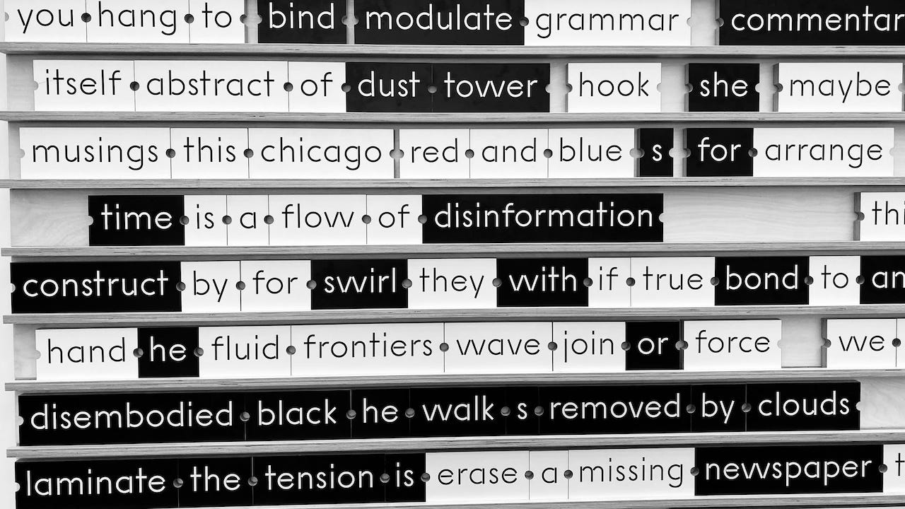 A wall installation features multiple rows of magnetic poetry-style word tiles in black and white. Words like “time is a flow of disinformation,” “construct by for swirl,” and “disembodied black he walks removed by clouds” appear across the rows. The words are arranged in poetic or fragmented phrases and separated by small dot markers. A wall installation features multiple rows of magnetic poetry-style word tiles in black and white. Words like “time is a flow of disinformation,” “construct by for swirl,” and “disembodied black he walks removed by clouds” appear across the rows. The words are arranged in poetic or fragmented phrases and separated by small dot markers.