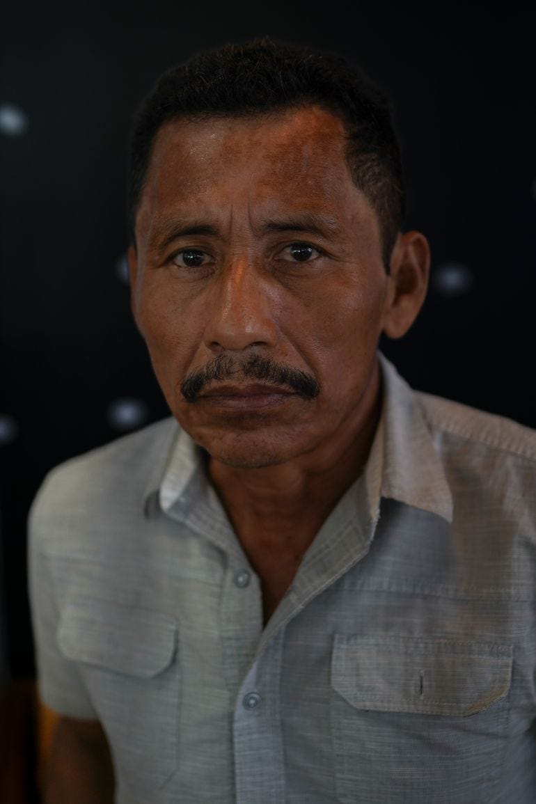 A middle-aged man with a mustache and a collared shirt stares into the camera.